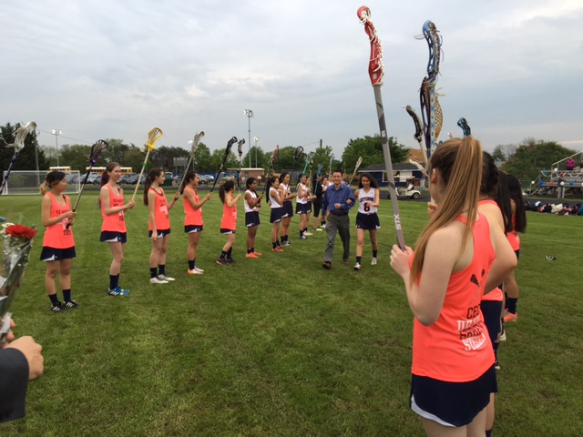 Senior lacrosse player Cece Xiao makes her way through the JV lacrosse team's path to accept a bouquet of flowers and handshake from Dr. Glazer.
