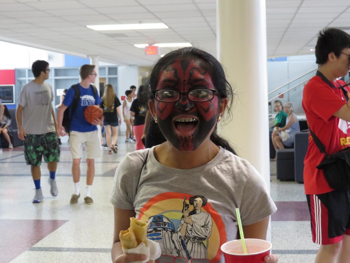 Sophomore Ankita Vadiala grins with a Star Wars t-shirt, face paint, and an armful of food and drink.