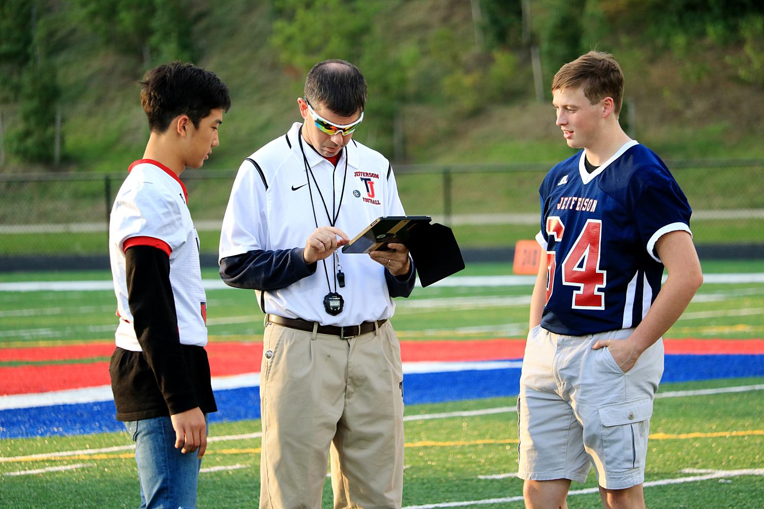 From left to right: Junior Jun Chong and Senior John Erskine discuss plans with teacher and football coach Michael Auerbach before the game starts.