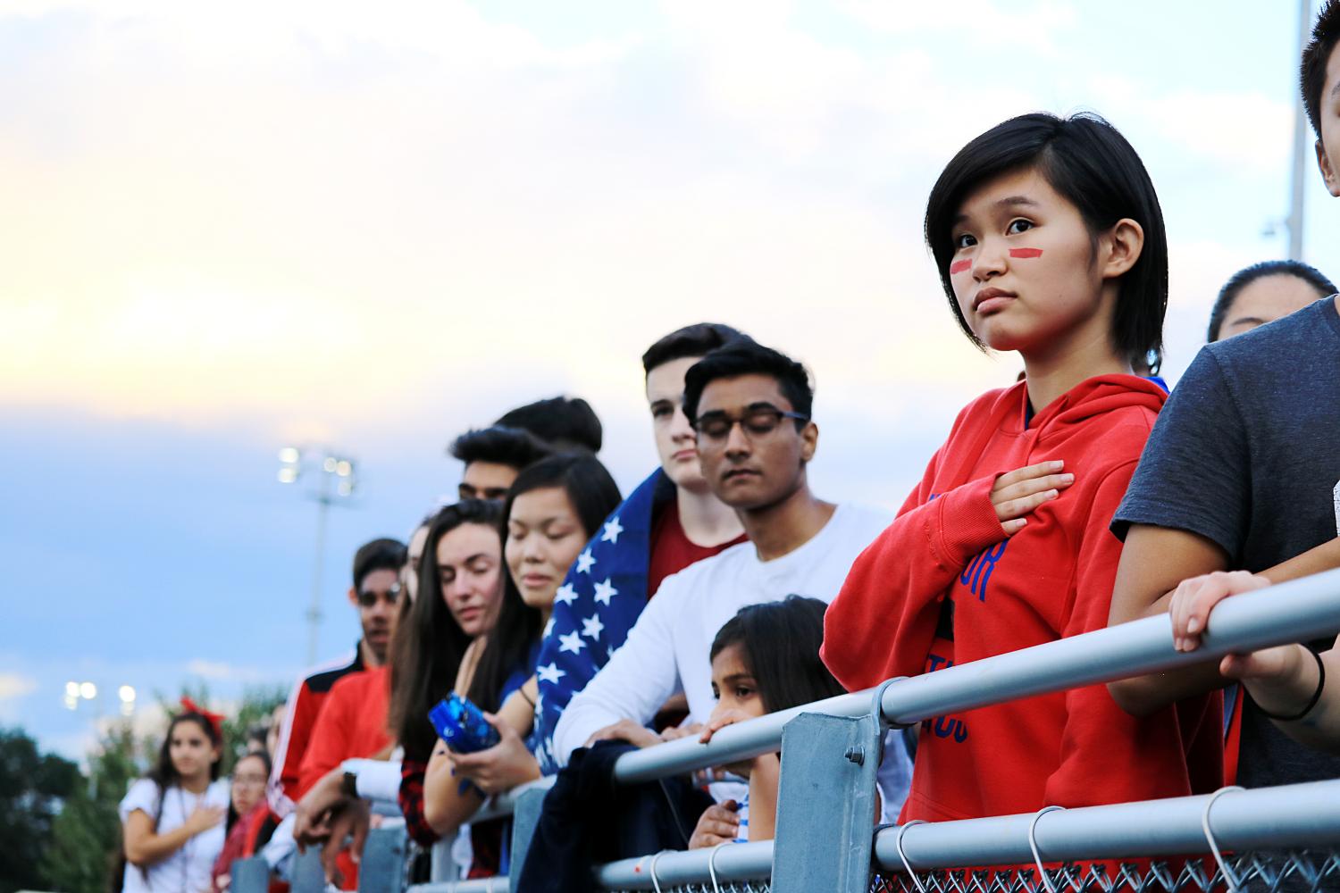 Junior Cynthia Zhang stands alongside others as the Star-Spangled Banner is performed by students on the track surrounding the football field.