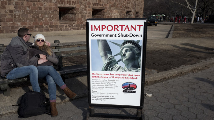 Photo courtesy of Mark Lennihan, Associated Press. Tourists rest on a bench on Sunday in lower Manhattan as they wait for the Statue of Liberty to re-open.