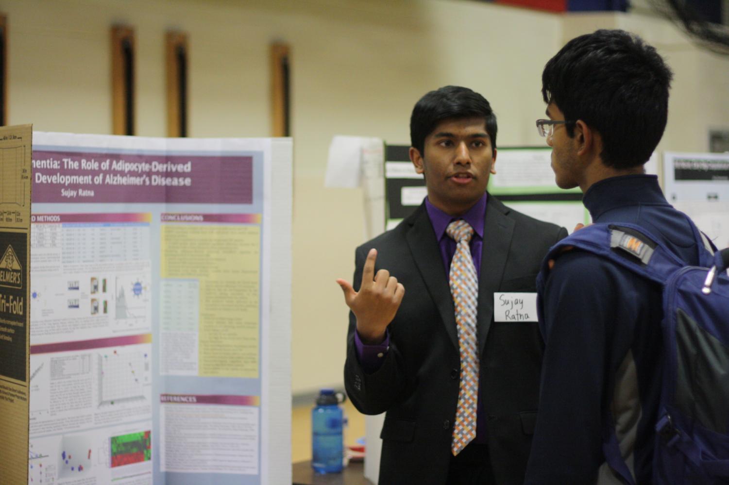Pointing to his poster, senior Sujay Ratna presents his research to a student. Ratna's project won in the category of Cell and Molecular Biology.