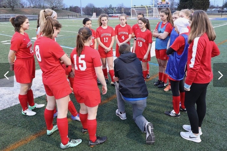 Freshman Lauren Spehlmann (far right, in red warmup jacket) stands with her teammates as the coach addresses the team.