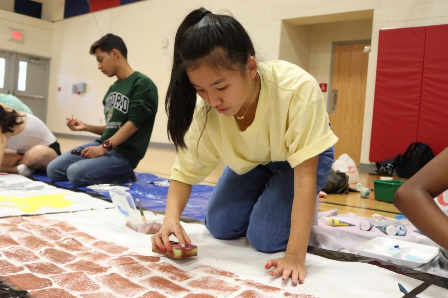 Junior Tammy Ding uses a sponge to paint bricks in the middle of 2021s banner. 2021s banner was a representation of various items on a filmstrip. Filmstrips are vintage, and we [wanted to] have different elements of the 90s in each picture, Ding said.
