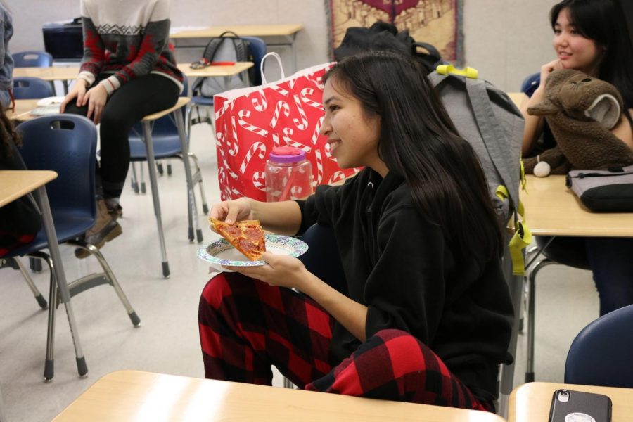Wearing pajamas to celebrate Friday’s Festive and Flannel Friday, junior Hailey Nguyen smiles and prepares to take a bite of her pizza.