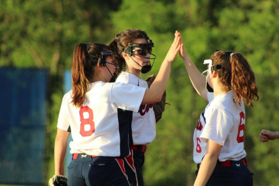 Girls on the 2019 softball team share a high five after a play. 