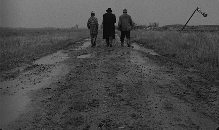 Sanyi (András Bodnár), Irimiás (Mihály Víg), and Petrina (Putyi Horváth) walking down one of many endless muddy roads in “Sátántangó”. Image courtesy of Filmgrab.