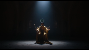 Dev Patel’s Gawain sits on a throne and has a crown lowered onto his head in the opening scene of “The Green Knight”.