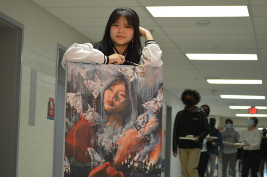 Shown in front of a crowd of people, senior Alice Ji stands with her acrylic self portrait, “When I start with a painting, I have one main subject that I want to be the focal point, and smaller things I want to draw with it. Paintings become a cluster of these two: Around the person, I like to have more fantastical elements,” Ji said. Several of her portraits focus on people due to the level of depth and detail she can invest into them, “As for what inspires me to create art, I paint people because I feel its a lot easier to express emotion or tell stories when there is a person in it. For me, its just the fundamental idea of making something that you love,” Ji said.
