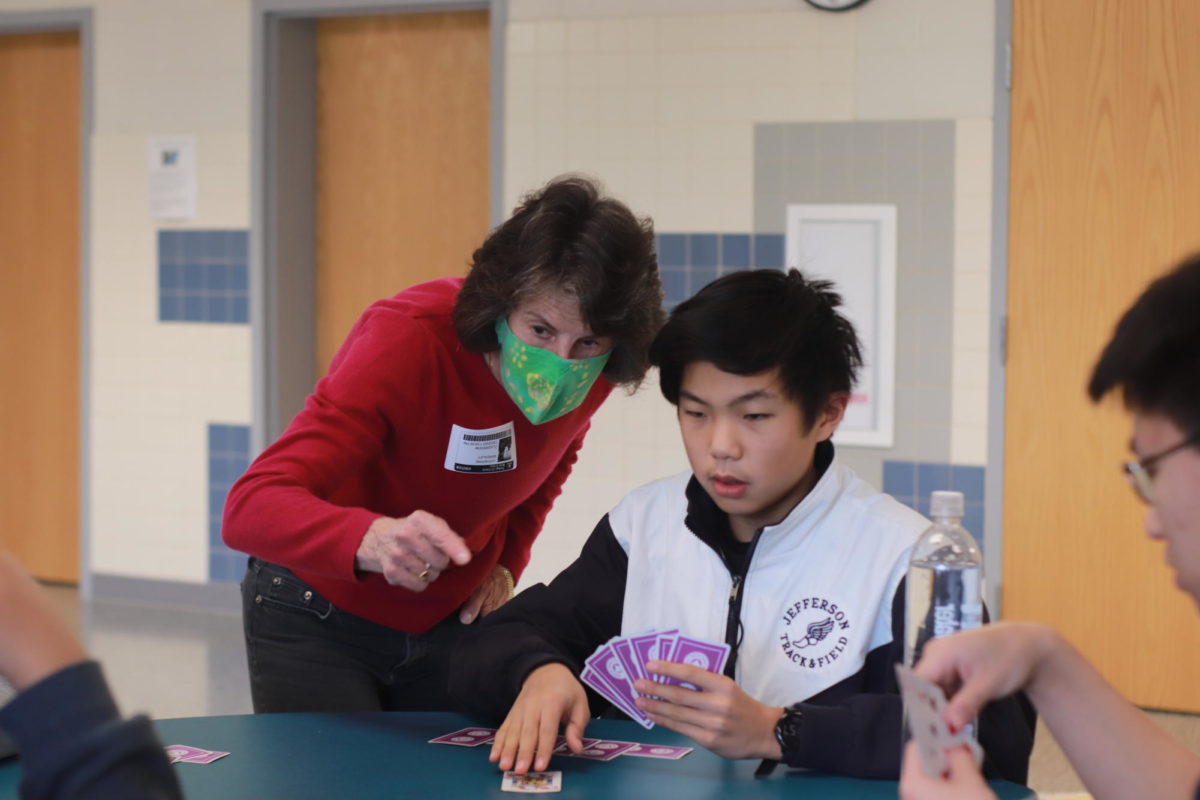  Leaning over a student’s shoulder, volunteer Catherine Bardsley points out the next steps during gameplay. By signing up for bridge club, Jefferson students show genuine interest in learning the game. “I find it fun watching people who are very quick to understand things, and yet who will be much better once they've had some experience playing. It's just fun to watch somebody learn something they're interested in,” Bardsley said. 