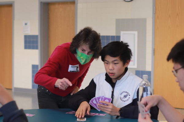  Leaning over a student’s shoulder, volunteer Catherine Bardsley points out the next steps during gameplay. By signing up for bridge club, Jefferson students show genuine interest in learning the game. “I find it fun watching people who are very quick to understand things, and yet who will be much better once they've had some experience playing. It's just fun to watch somebody learn something they're interested in,” Bardsley said. 