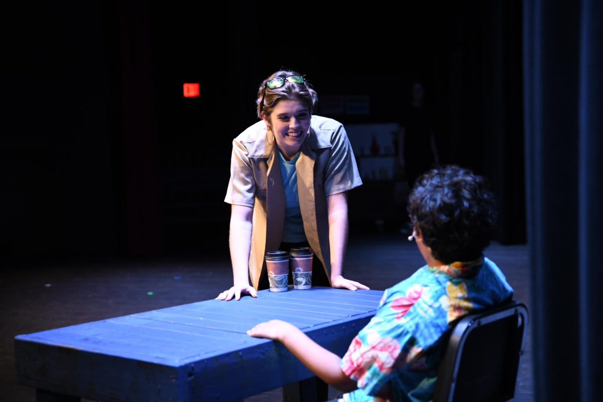 During "Callback," junior Ella Tysse, playing Cam, leans eagerly over a table to talk to freshman Vyaas Raj, who plays Reuben. “Here, Cam is asking for directions as she and Robin make a pitstop, and Reuben is the head of the tourist shop for Nebraska’s largest ball of twine,” senior Mayuka Valluri said.