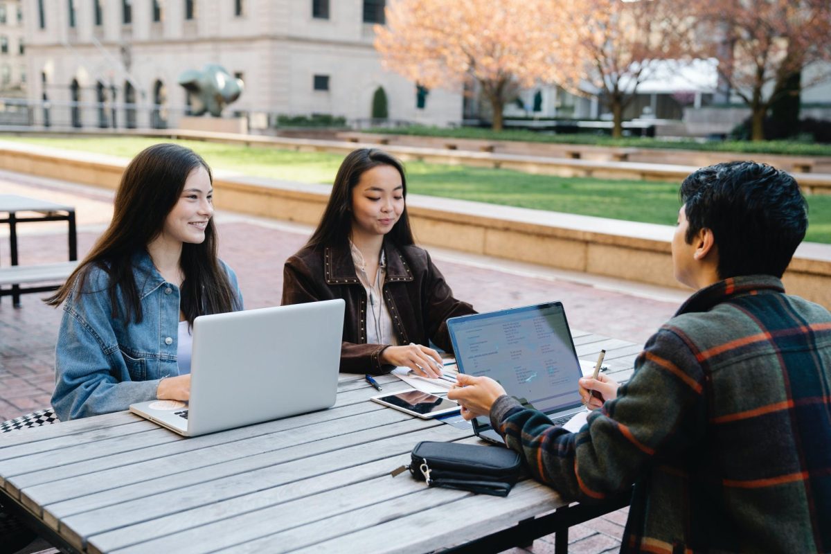 Three students sit on a desk working on assignments. With AI being an easily accessible tool, it is important for students to understand it's proper usage in regards to schoolwork.