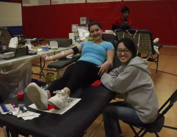 Pictured next to senior Gloria Bao with phlebotomist Mohammad Katawazai seen in the back, senior Demetra-Aurora Tudorache gets her blood drawn. “I was a little nervous because I didn’t want to faint, that was a big issue for me. But the volunteers were super nice, super knowledgeable, Tudorache said. They told me everything step by step, so it was totally fine.