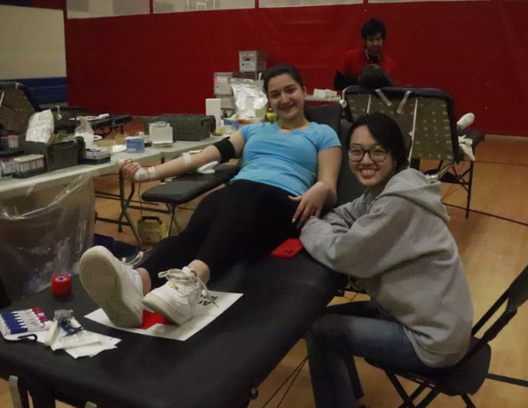 Pictured next to senior Gloria Bao with phlebotomist Mohammad Katawazai seen in the back, senior Demetra-Aurora Tudorache gets her blood drawn. “I was a little nervous because I didn’t want to faint, that was a big issue for me. But the volunteers were super nice, super knowledgeable," Tudorache said. "They told me everything step by step, so it was totally fine."