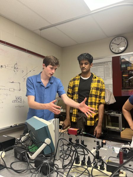 Gesturing towards their project, senior Alec Riso describes the mechanisms of the group’s QKD system alongside senior Karthik Thyagarajan. “This laser generates a stream of photons. We lined it up with a collimated lens, [which] focuses the laser into an optical fiber,” senior Connor Whiting said. “The optical fibers [preserve or maintain] are how you measure the polarization state of the photon, which lets us do the encryption protocol.” 