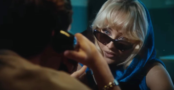 In prison, Sabrina Carpenter talks on the phone with Barry Keoghan during the "Please Please Please" music video.