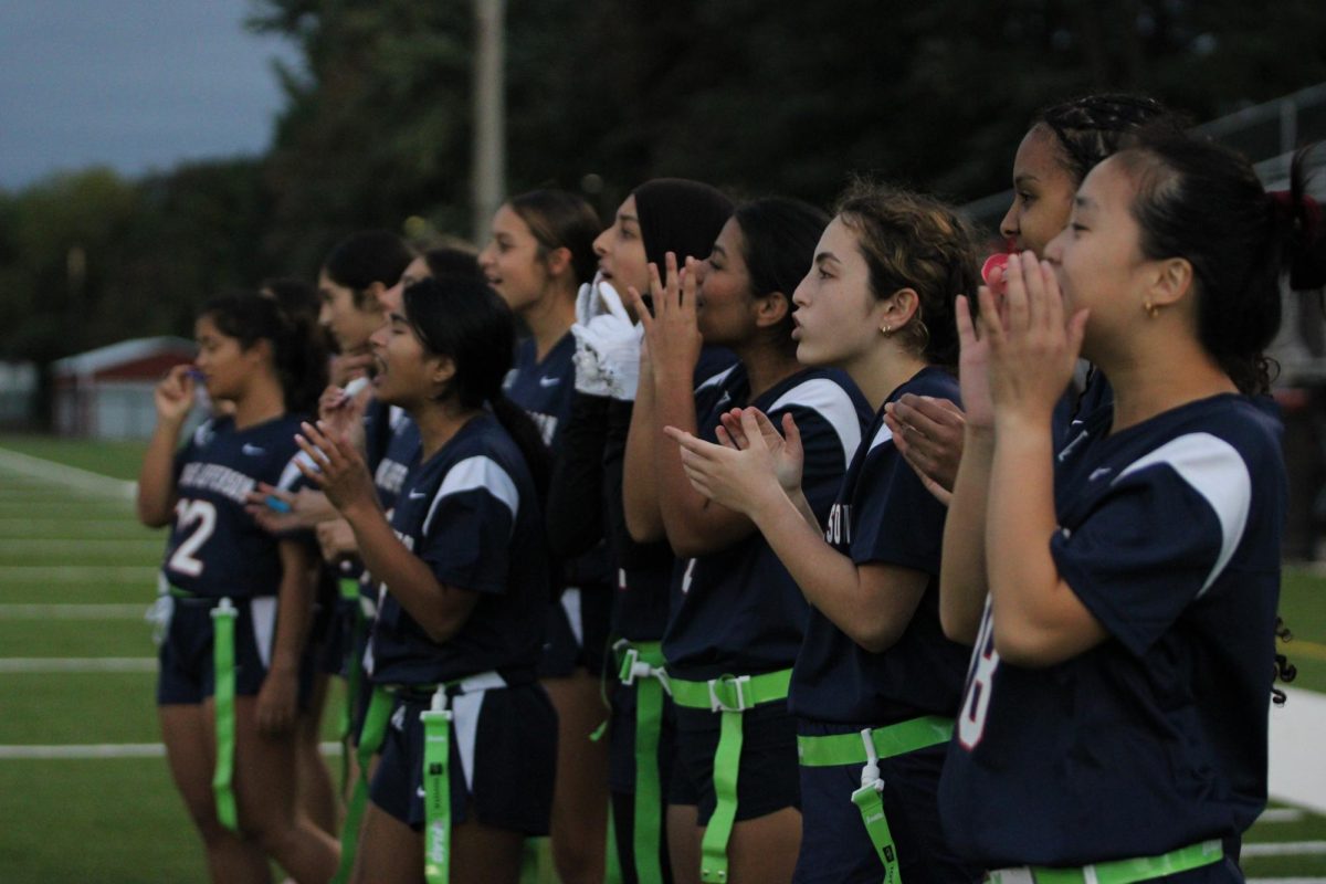 Cheering from the sidelines, the girls flag football team encourages their offense during the first half of their game against the Lewis Lancers on Oct. 14. “[We’re going to] continue to put an effort into our practices and games every single play,” Palle said. “[We will try to] get better at our plays, execute them better and just hustle a lot on defense.”