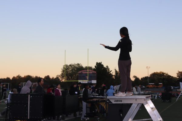 Senior drum major Grace Bai stands on a podium while conducting the marching band during an after-school practice. Bai conducted the first two parts of the show at the 36th annual Oakton Classic on Oct. 18. “In order to lead the band musically, we [have to] keep the band together,” Bai said.